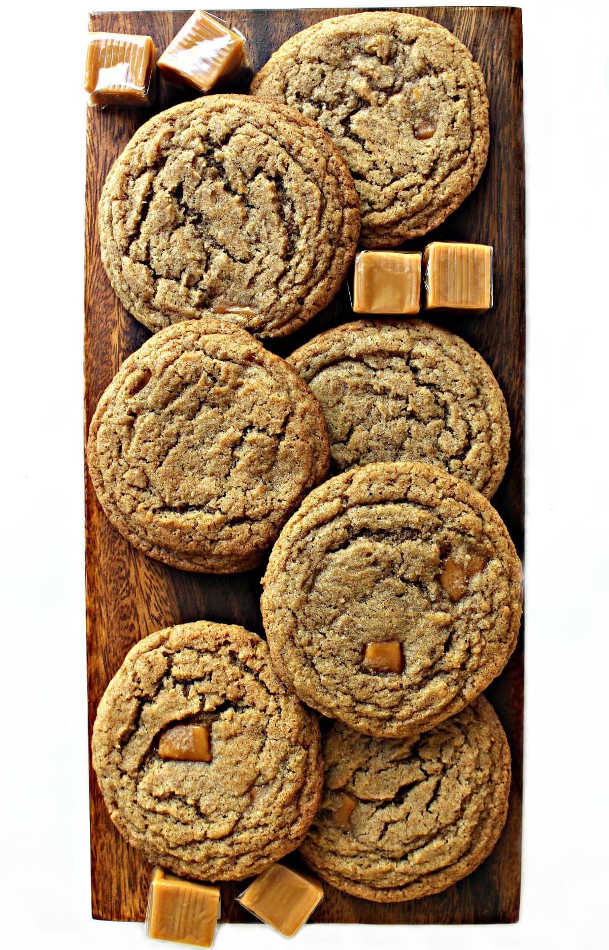 Thin, crinkled Whole Wheat Caramel Cookies on a wooden cutting board with caramel squares.