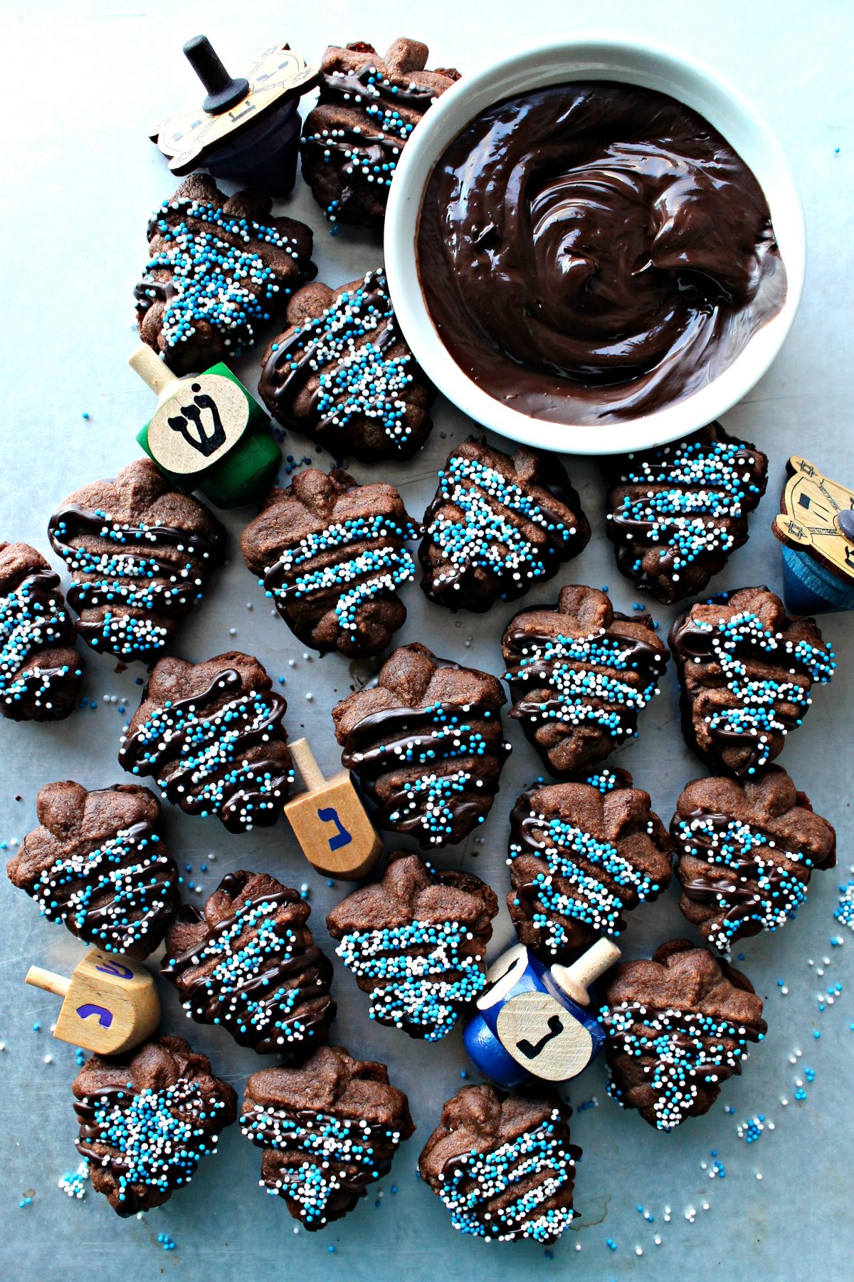 Chocolate cookie press cookies shaped like dreidels, sandwiched with chocolate, sprinkled with blue and white nonpareils.