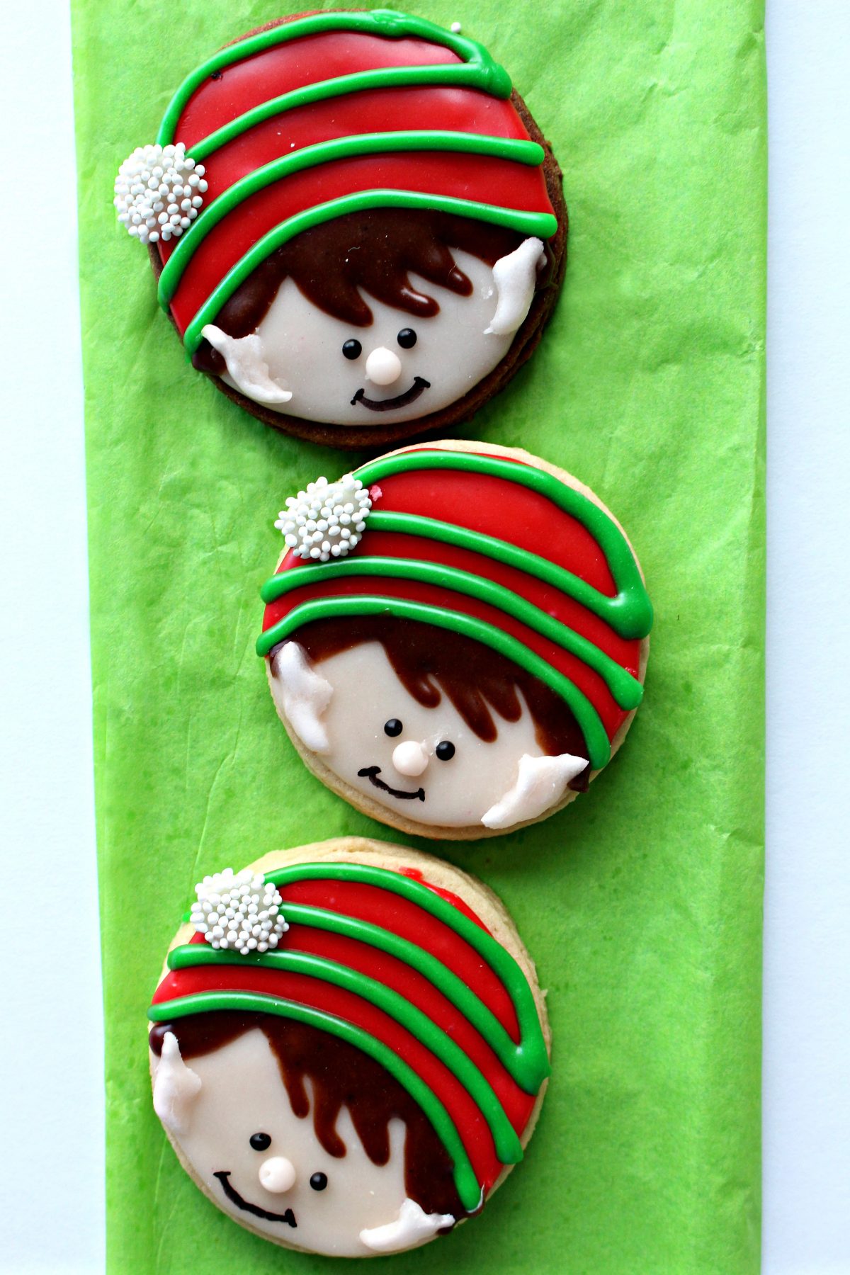 Three elf cookies with faces and red and green stocking caps.
