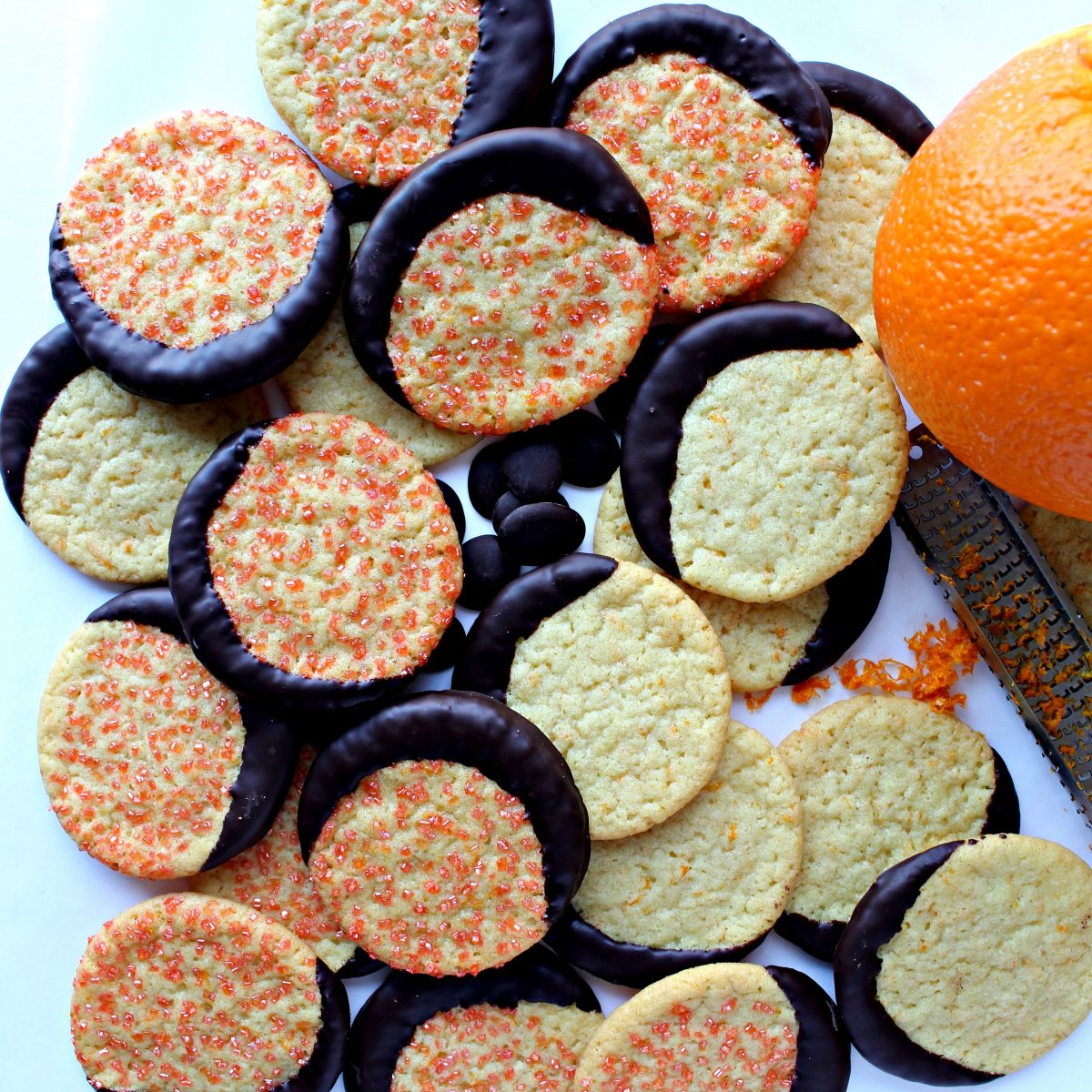 Cookies, some with orange sugar and dipped in chocolate, next to an orange and microplane zester.