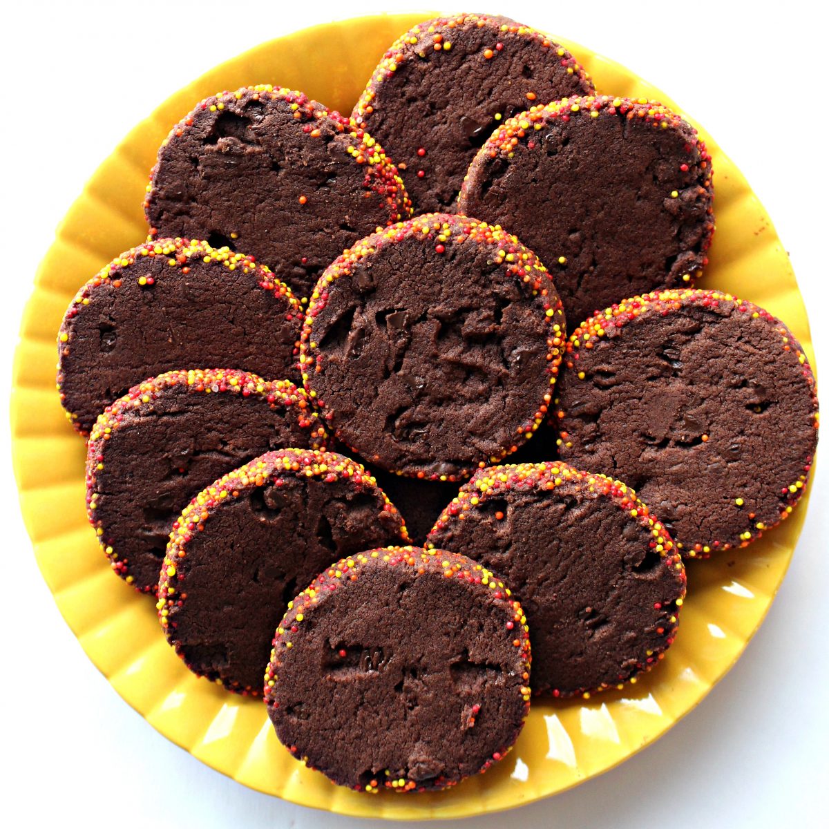 Sliced chocolate shortbread cookies with nonpareil sprinkles on their edges on a  plate.