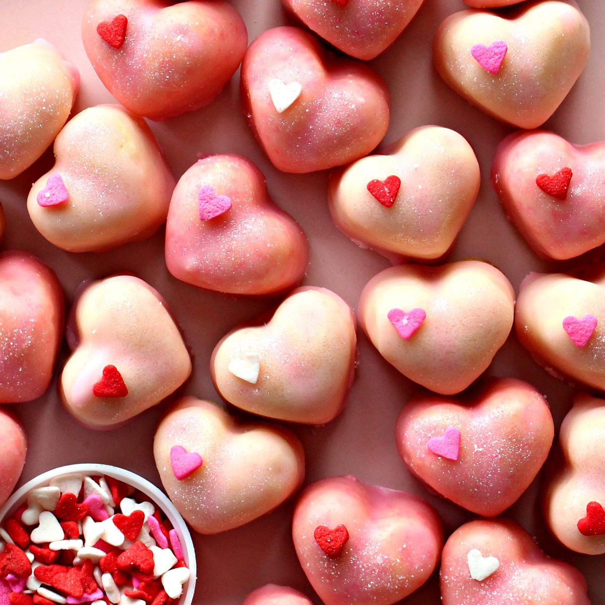 Closeup of heart shaped molded cookies, iced pink with one heart sprinkle.