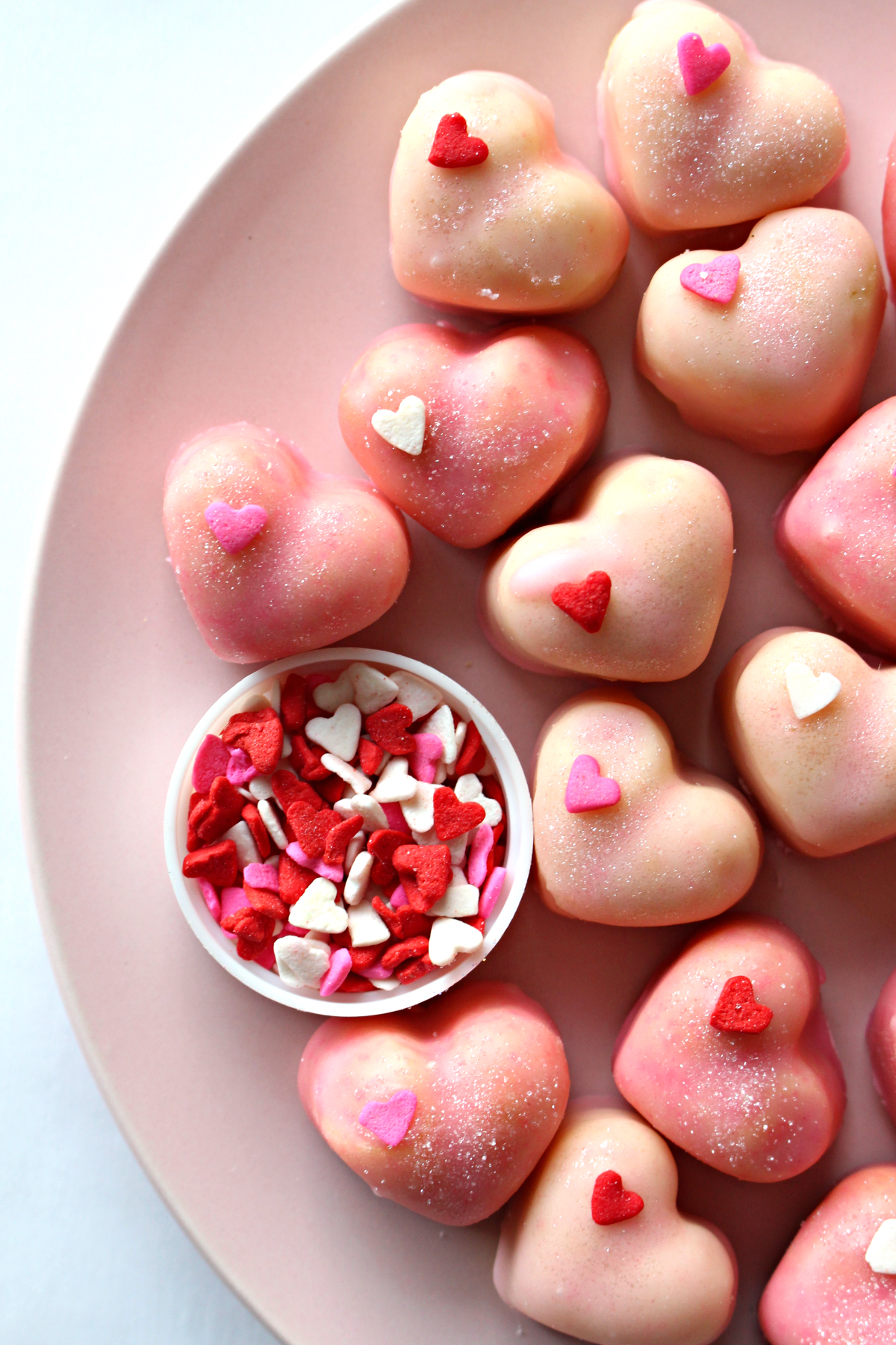 Closeup of cookies on a pink plate with a cup of heart sprinkles.