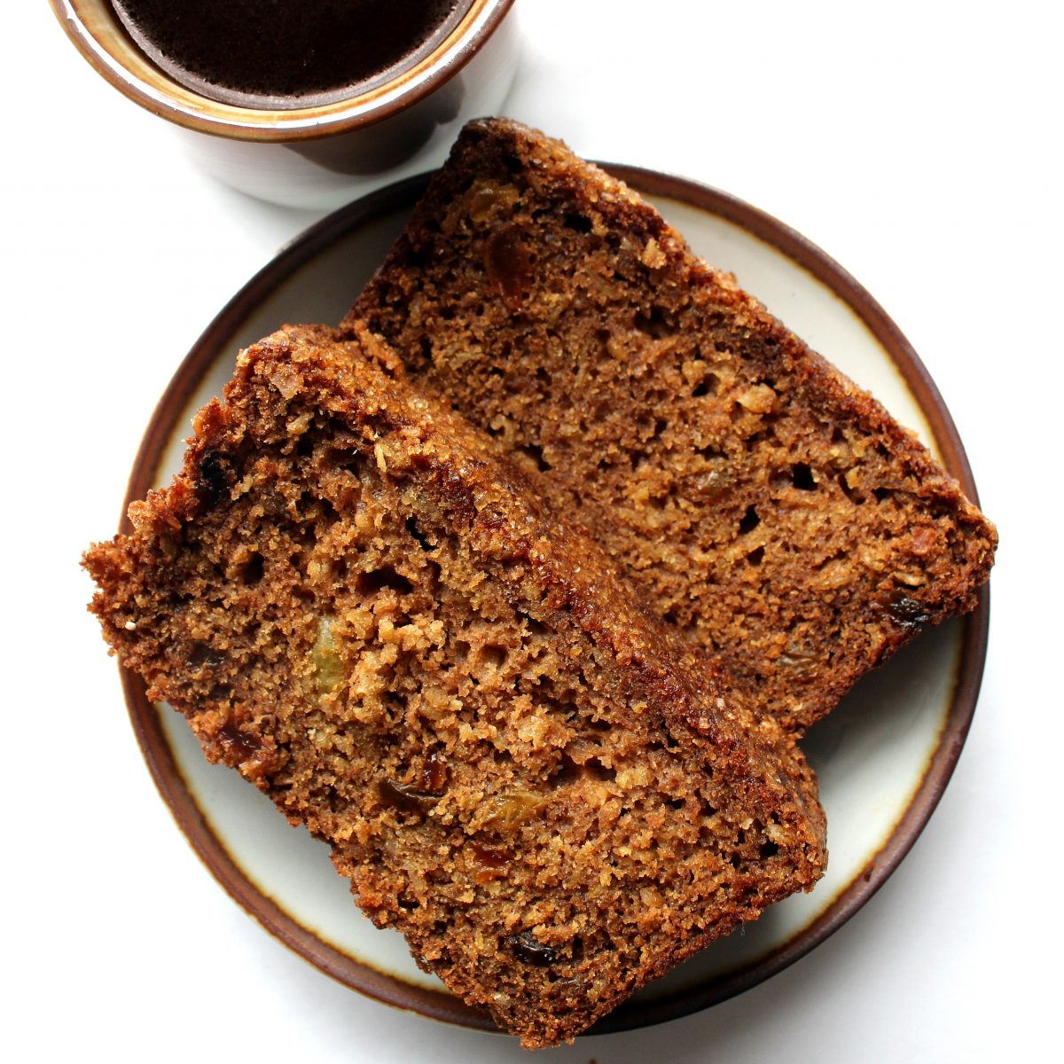 Two slices of oatmeal bread on a plate next to a coffee mug.