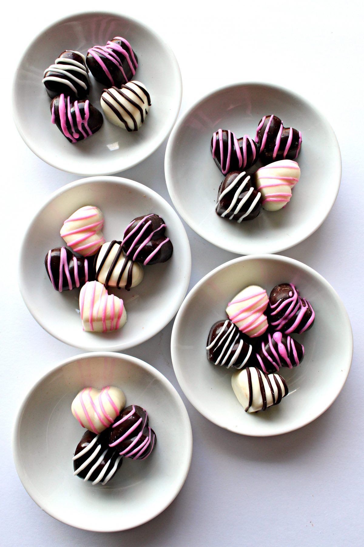 Five small white plates with a few hearts in white and dark chocolate decorated with stripes.
