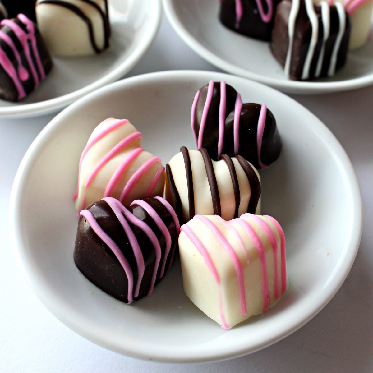 Closeup hearts in white plate in dark and white chocolate with pink or chocolate stripes.