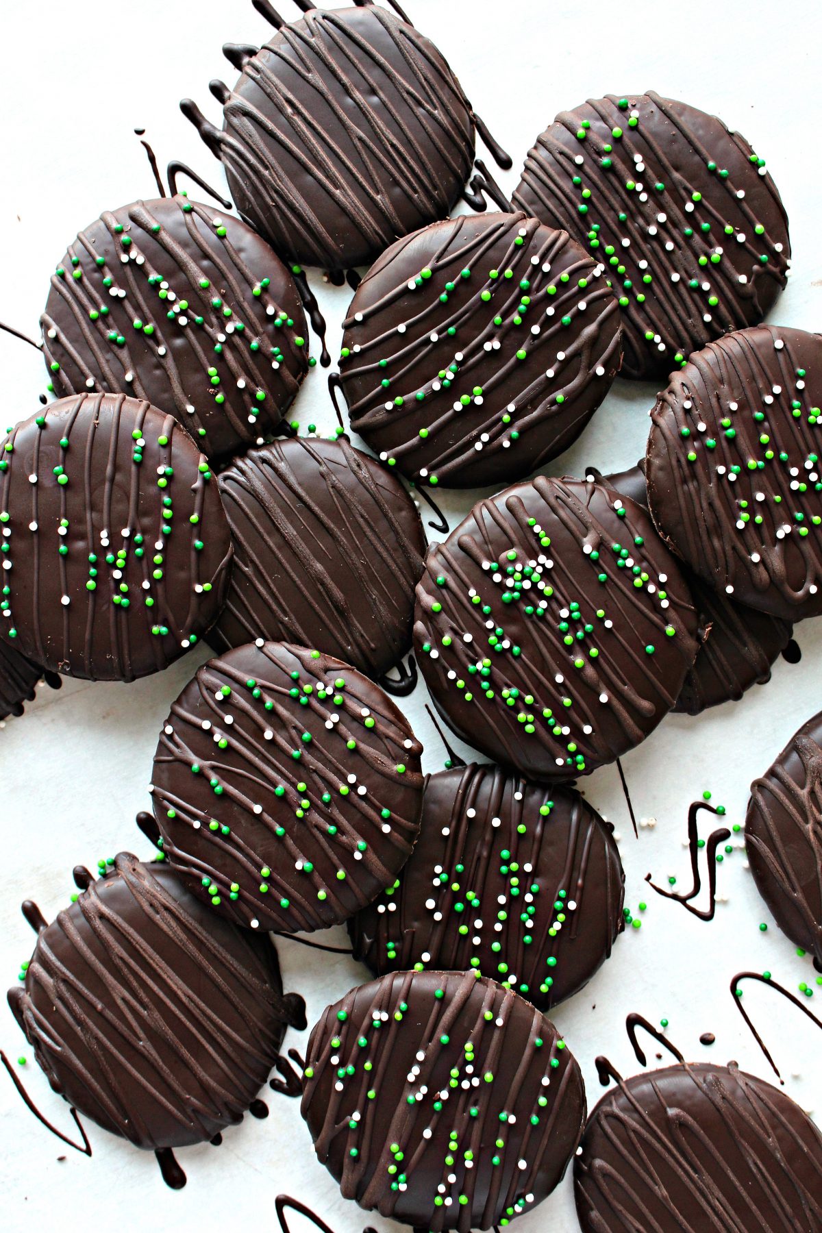 Chocolate Covered Chocolate Mint Cookies are decorated with chocolate zigzags and green and with nonpareil sprinkles.