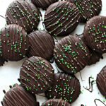 Cookies coated in chocolate topped with chocolate drizzle and sprinkles.