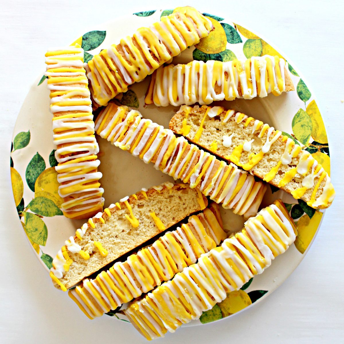 Lemon Biscotti with yellow and white icing zigzags on top, on a plate. 