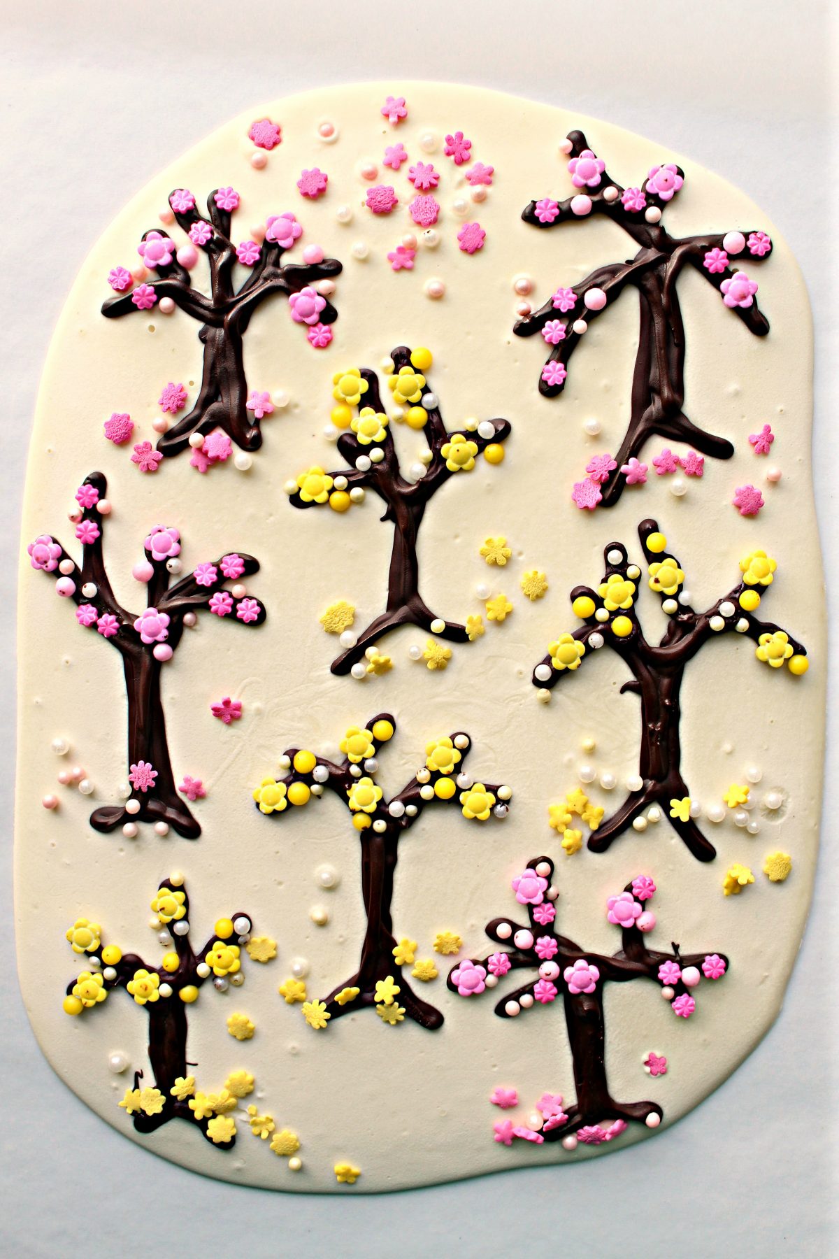 White Chocolate Bark  with white chocolate background, piped chocolate trees, and pink and yellow sprinkle blossoms. 