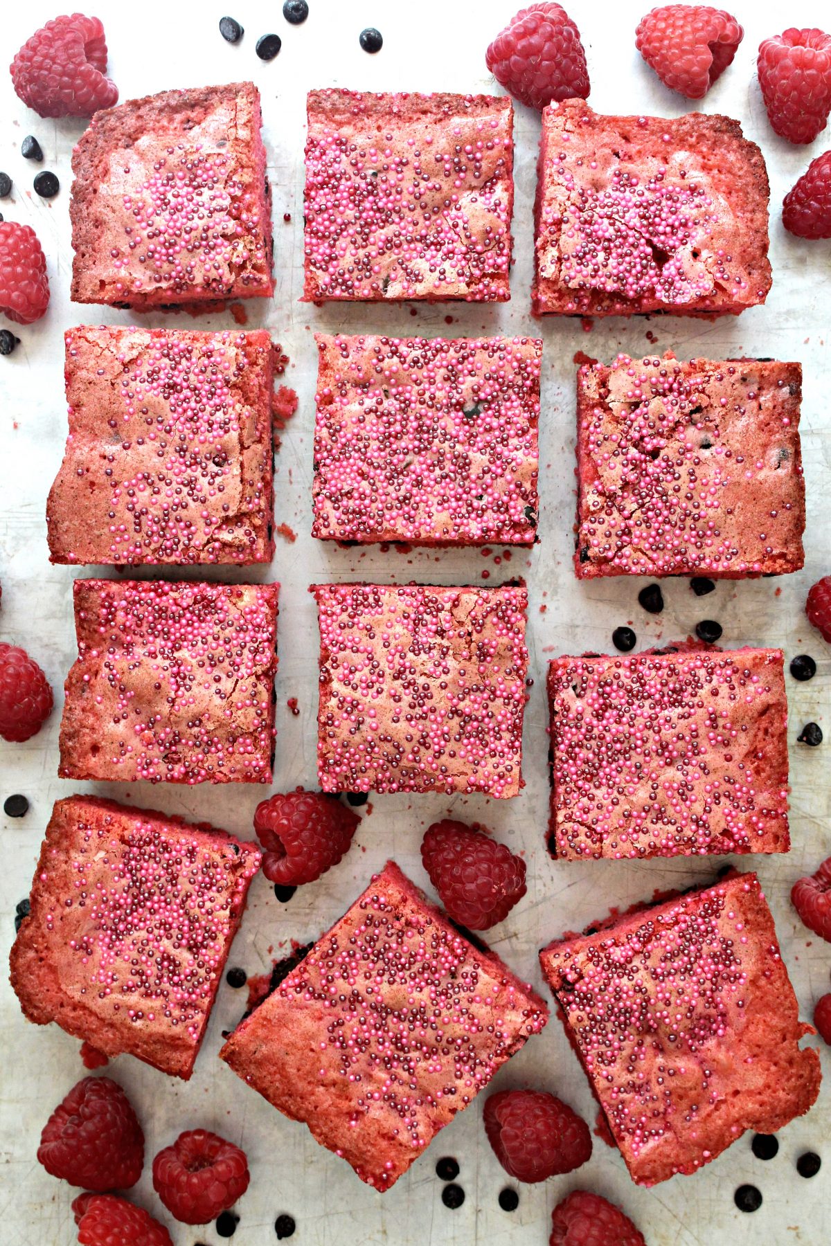 Raspberry Chocolate Chip Bars cut into squares on background sprinkled with chocolate chips and raspberries.