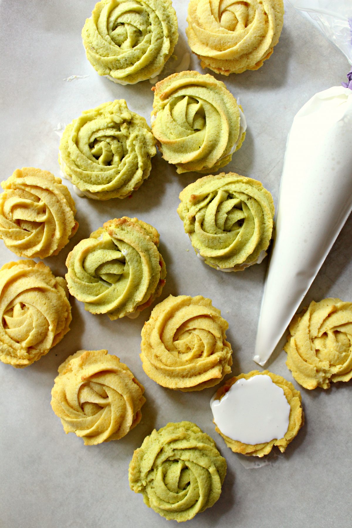 Lemon and Lime Butter Cookie Rosettes on gray background with a piping bag of white icing.