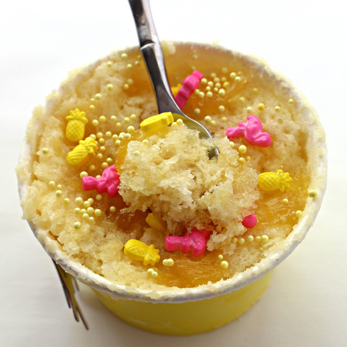 A spoon scooping pineapple mug cake out of a paper snack cup.