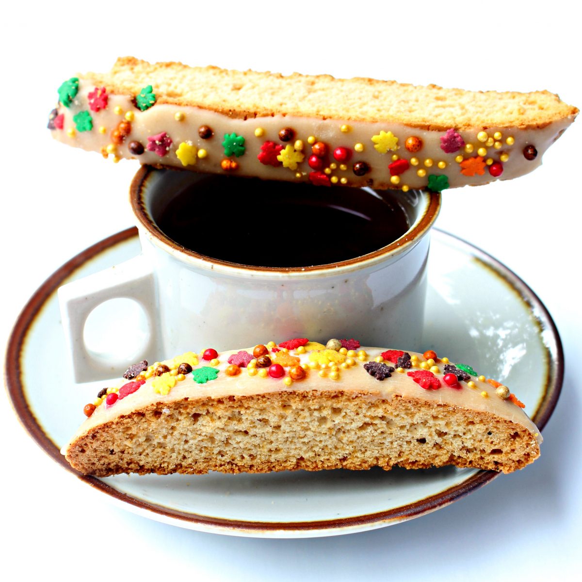 Two biscotti, one on a coffee mug rim and one on the saucer.