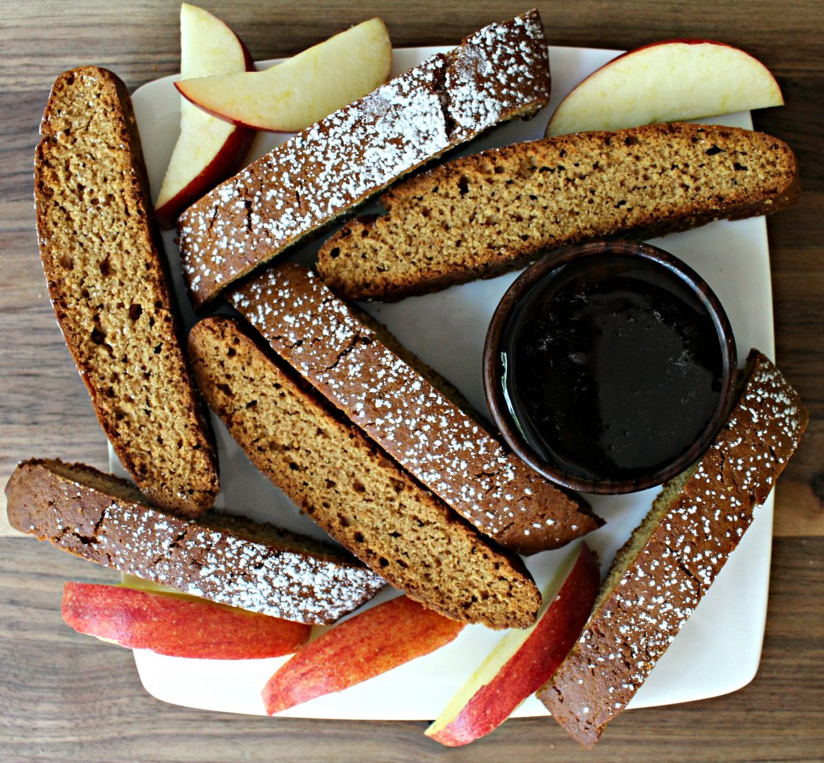 Overhead view of biscotti, apple slices, and a bowl of honey on a white plate.