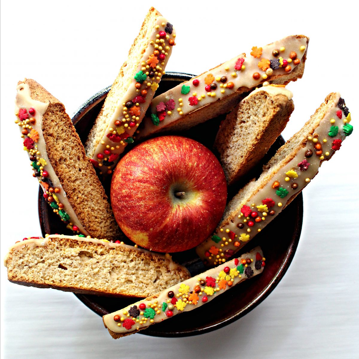 Iced Biscotti with fall leaf and pearl sprinkles in a brown bowl with an apple.