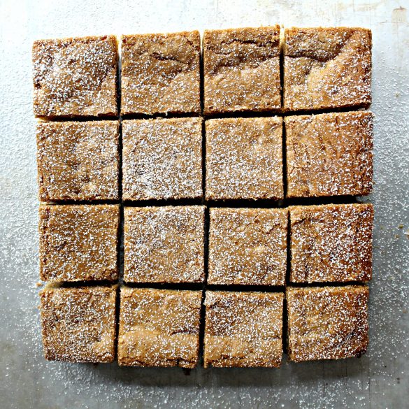 Root Beer Float Bars are chewy, sweet, and full of fragrant spices that make them warm and welcoming. Sassafras, winter green, cinnamon, and allspice are a magical combination!| themondaybox.com #themondaybox #rootbeer #barcookie Pan of Root Beer Float bars cut and sprinkled with powdered sugar on a cutting board.