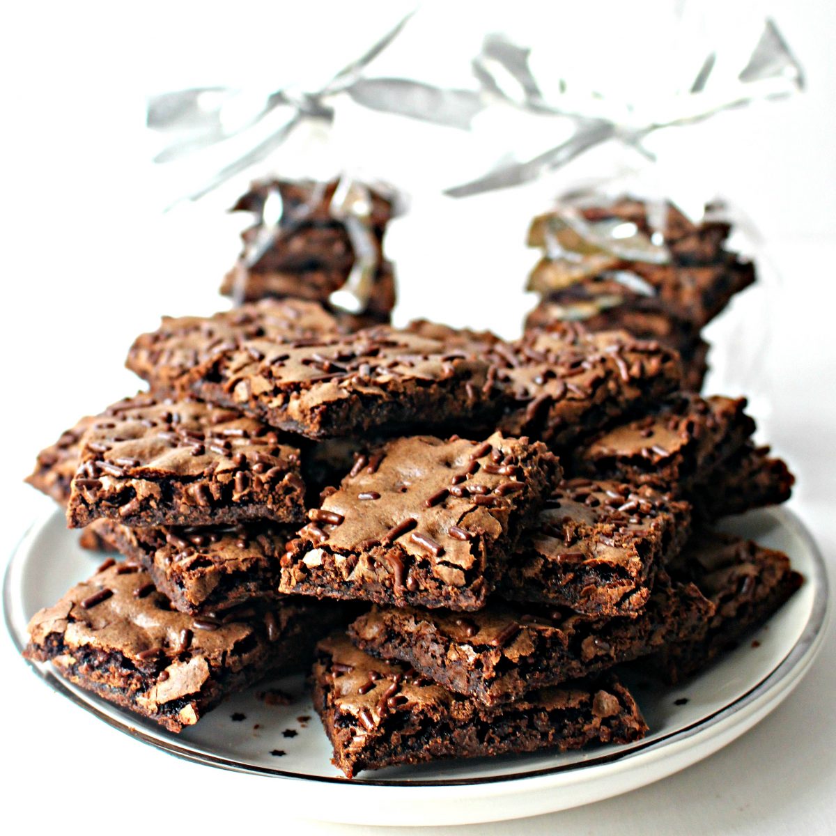 Piles of Malted Milk Brownie Bark on a white plate with two wrapped stacks of bark in the background.