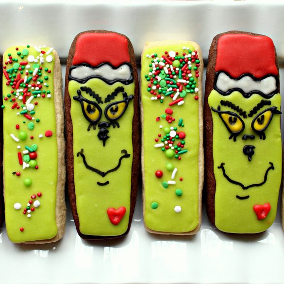 Two Grinch cookie sticks and two green sprinkled cookie sticks on a white plate.