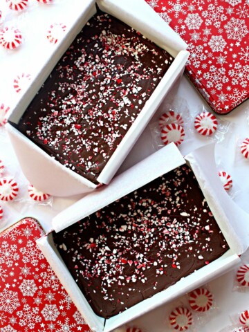 Two open tins filled with Peppermint Fudge, next to the red and white lids.