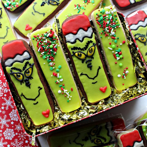 Four Decorated Grinch Cookies in a gift tin filled with shredded gold mylar.