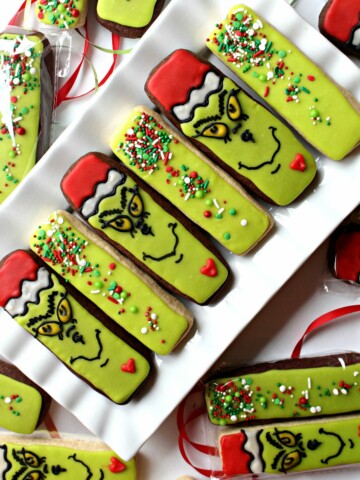 Diagonal photo of Decorated Grinch Cookies and Green Sprinkled Cookies on a white platter.