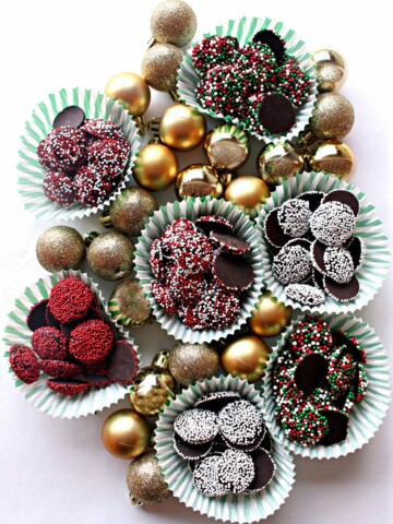 Gold ball ornaments and cups of Nonpareil chocolate candies coated in different colored sprinkles.