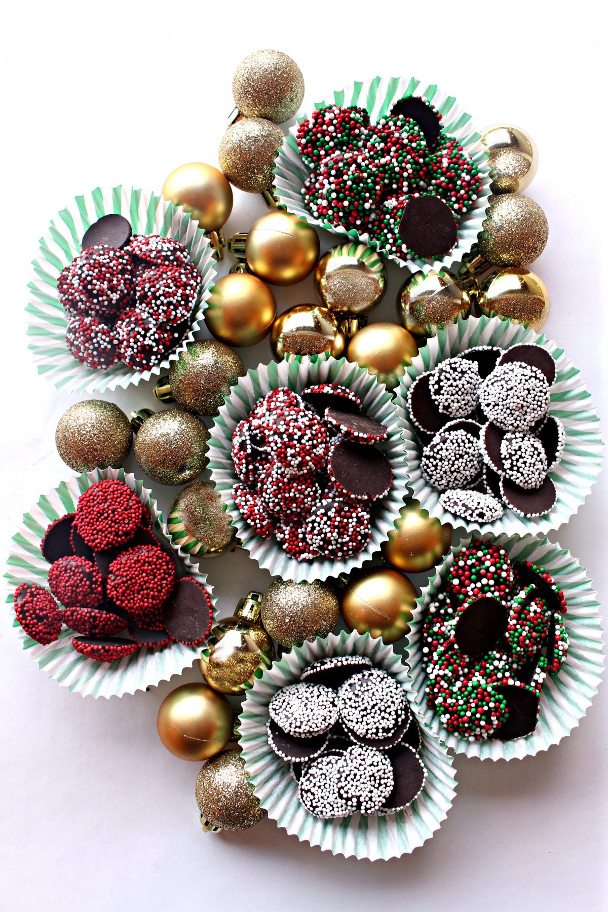 Gold ball ornaments and cups of Nonpareil chocolate candies coated in different colored sprinkles.