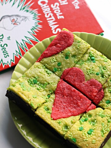 Green Grinch Brownies with a red heart on top on a green plate next to book.