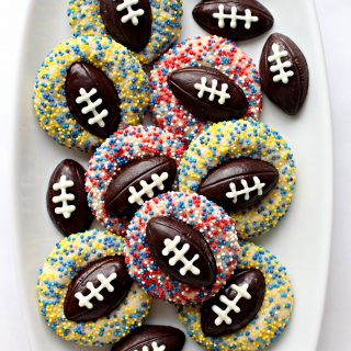 Shortbread Thumbprint Cookies with chocolate footballs in the thumbprint and sprinkles on each cookie.