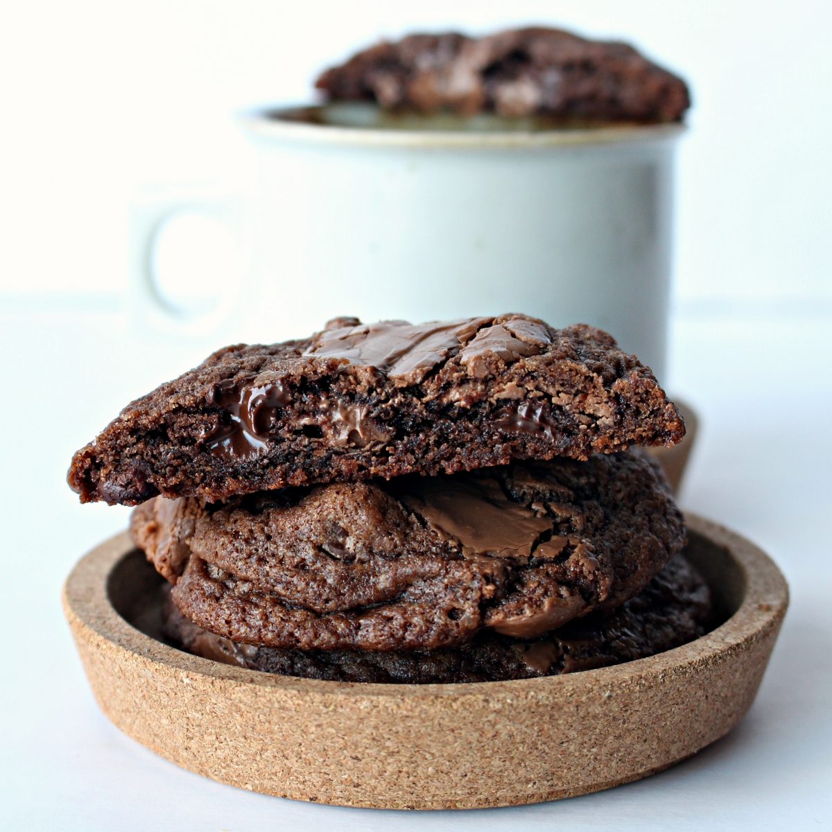 Stack of chocolate cookies with melted chips on a round cork dish.