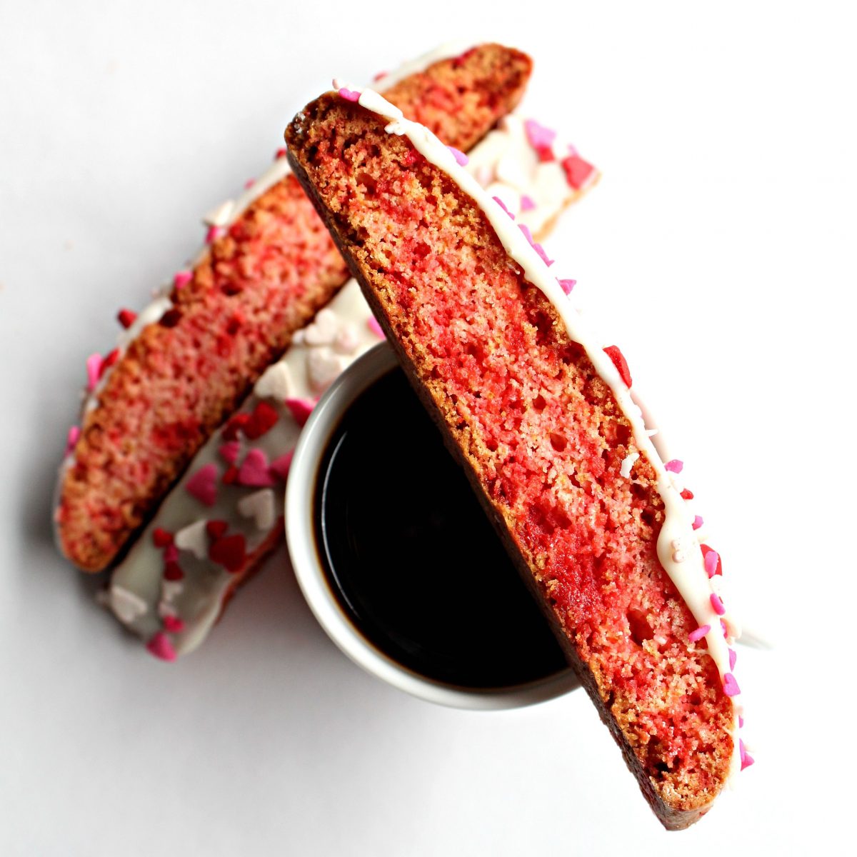 Pink and red biscotti balanced on top of an espresso mug.