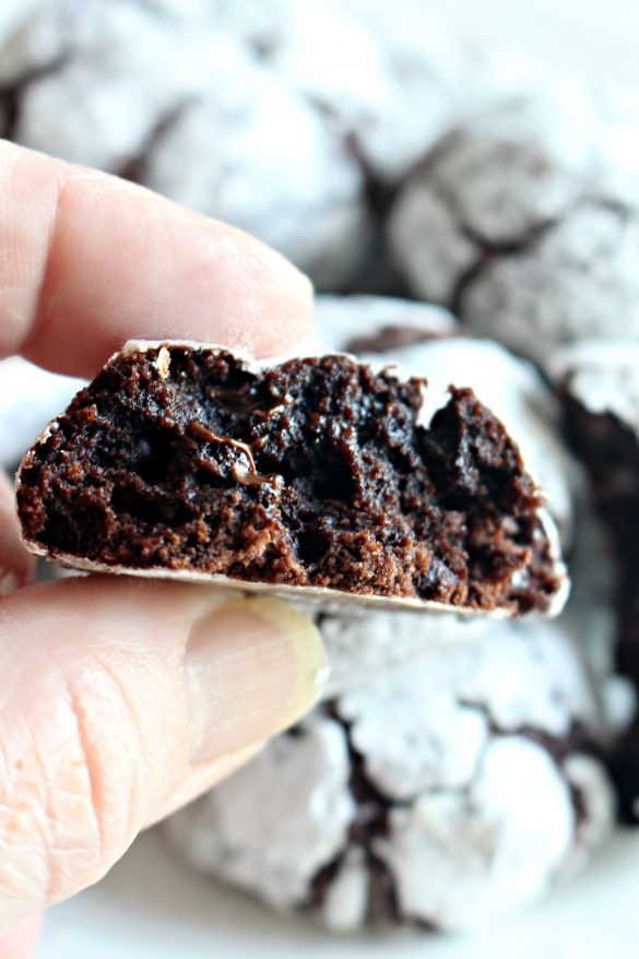 A hand holding half of a Chocolate Crinkle Cookie showing the fudgy interior.