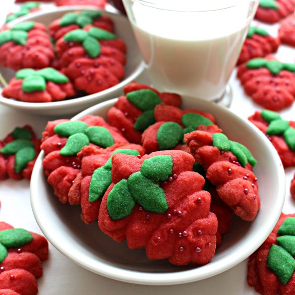 Red Strawberry Press Cookies with green dough leaves in white bowl with glass of milk 