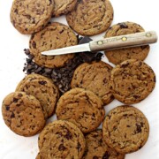 Chocolate Chip Molasses Cookies on a white background with a small knife and chopped chocolate