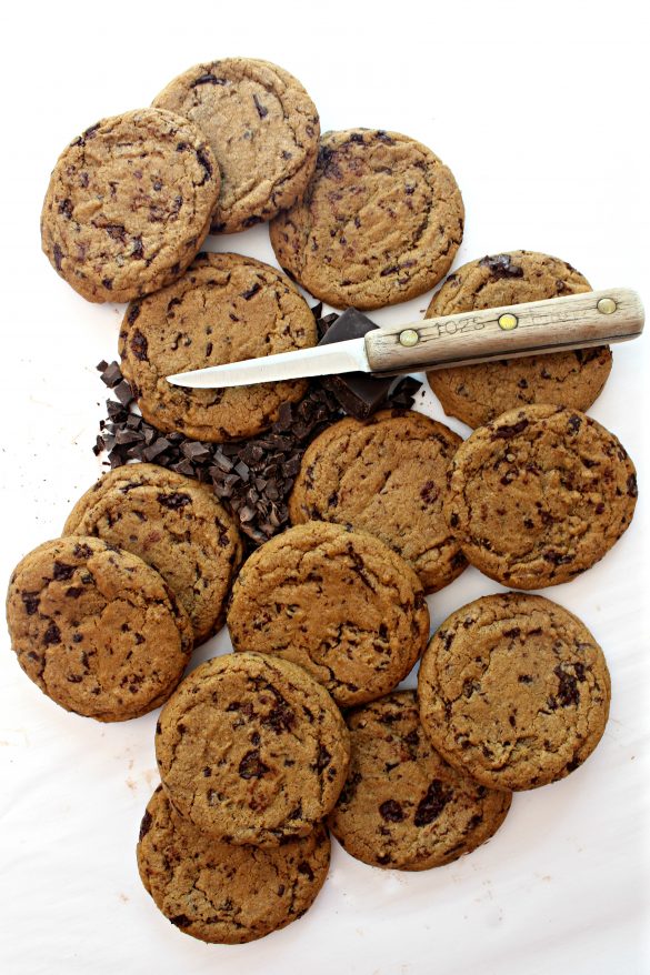 Round, brown Chocolate Chip Molasses Cookies on a white background with a small knife and chopped chocolate