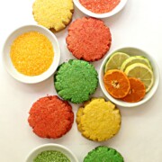 sugar cookies on white background with white bowls of colored sugar and sliced citrus fruit