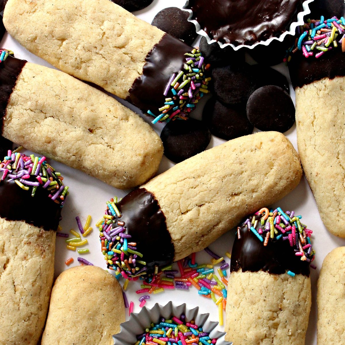 Closeup of finger shaped cookies with one end chocolate dipped with multicolored pastel sprinkles.