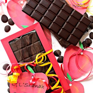 Unmolded chocolate bar next to chocolate bar inside red gift box surrounded by red apple shaped gift tags
