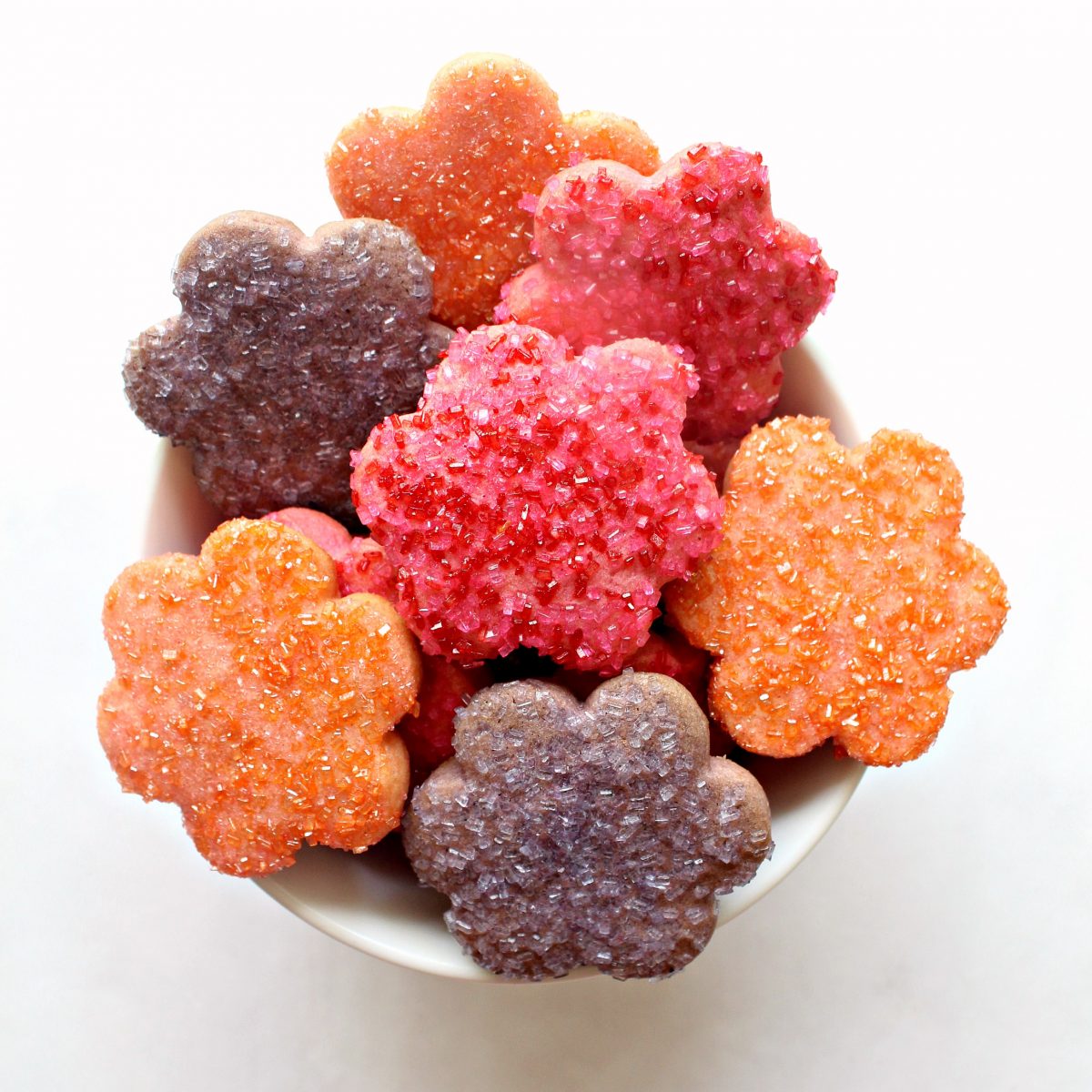 A bowl filled with orange, pink, and purple cookies cut out in daisy shapes.