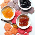 Colorful cookies in flower shapes with bowls of jam.