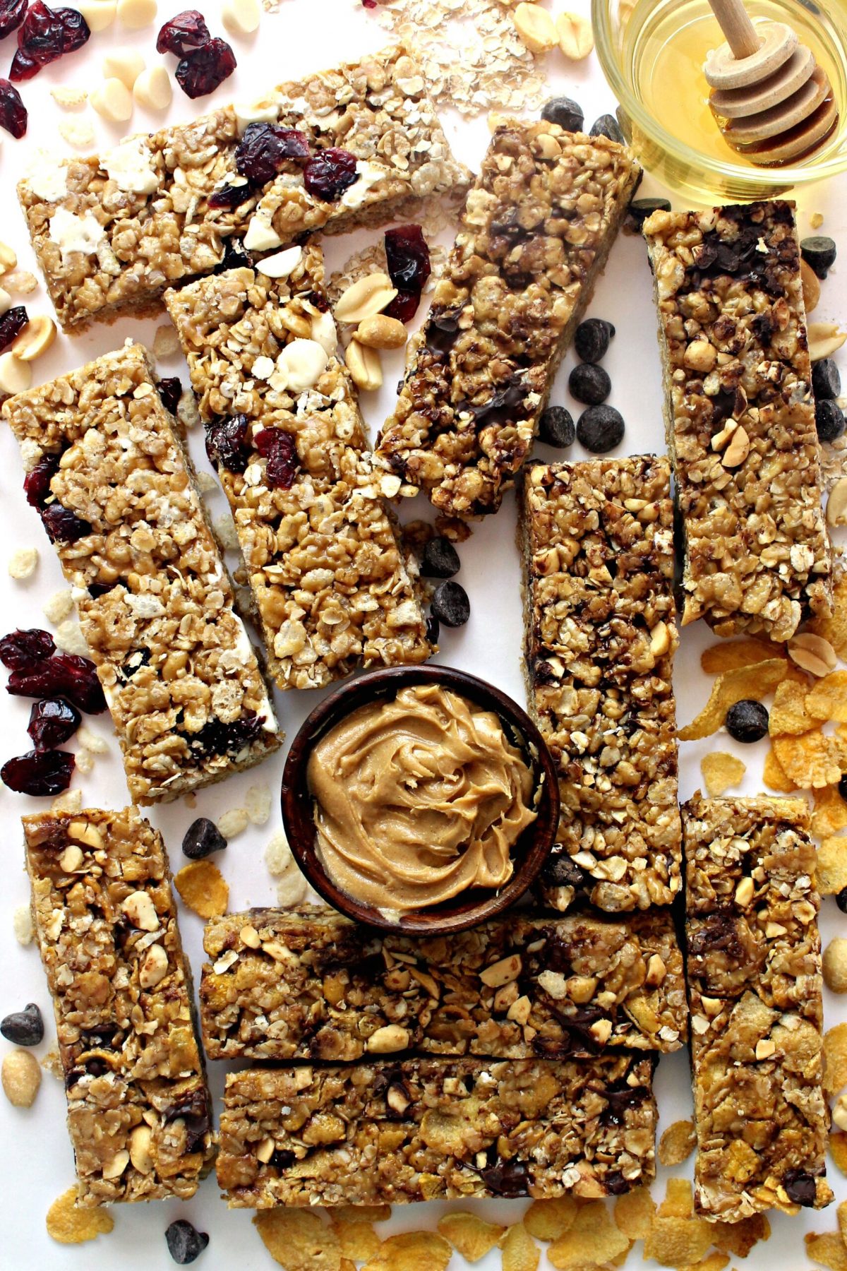 Granola bars surrounded by peanut butter, honey, oats, corn flakes, and cranberries.