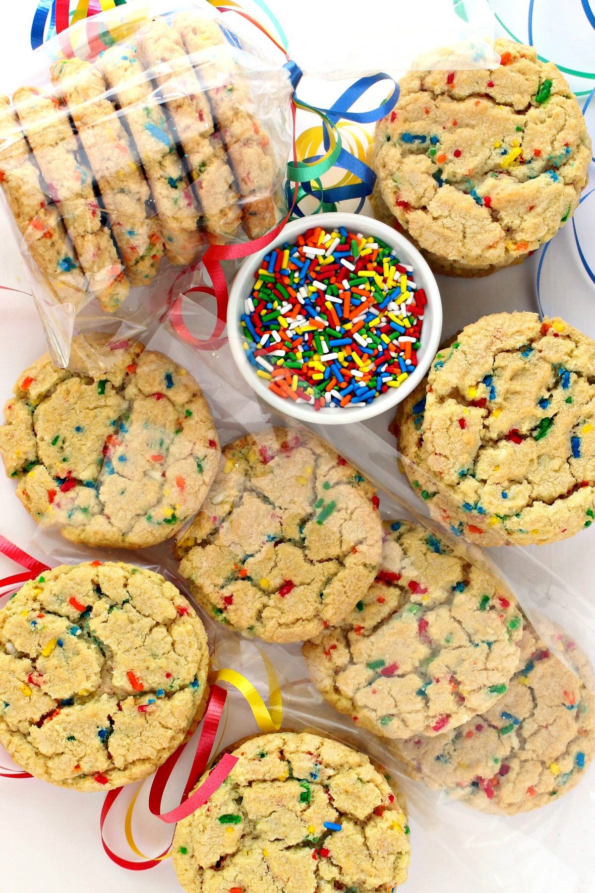 Funfetti Sugar Cookies, with rainbow sprinkles, a bowl of sprinkles and cookies wrapped in  clear cellophane bags. 
