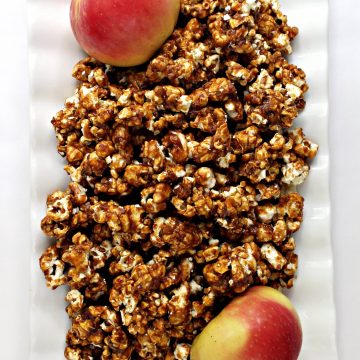 A white serving tray filled with Apples and Honey Caramel Popcorn and two apples
