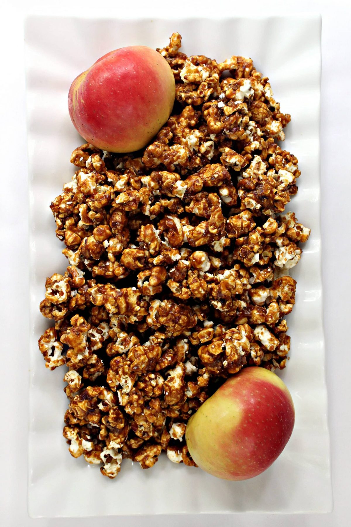 A white serving tray filled with Apples and Honey Caramel Popcorn and two apples.