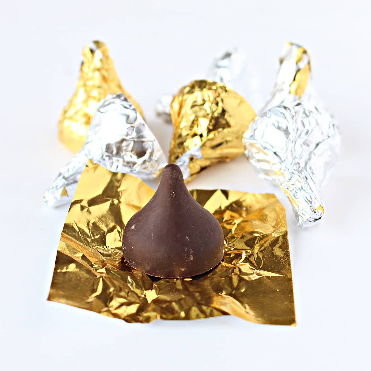 Chocolate kiss on a square of gold foil with foil wrapped kisses in the background.