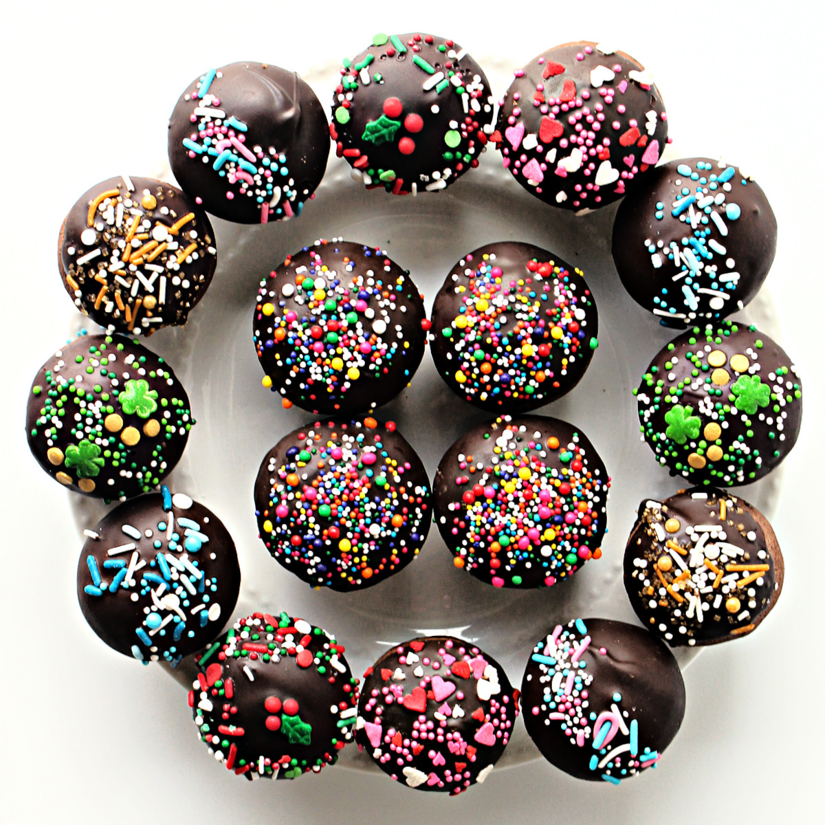 Balls of chocolate cookies each dipped in chocolate and topped with holiday sprinkles.