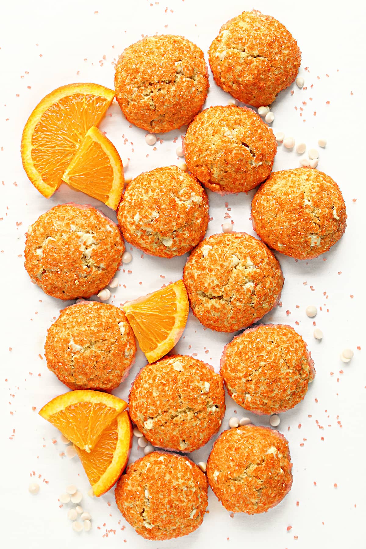 Cookies covered in orange sugar on a white background with orange slices, sugar, and white  chips.