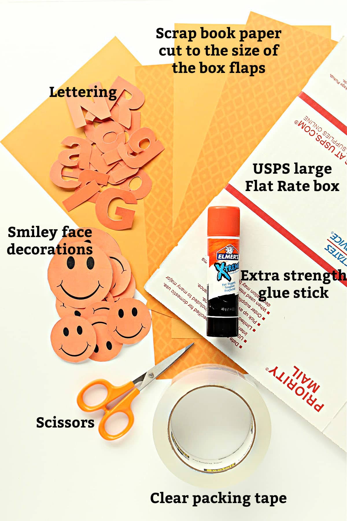 Box decorating supplies; box, glue stick, scissors, packing tape, orange paper, orange lettering, smiley decorations.