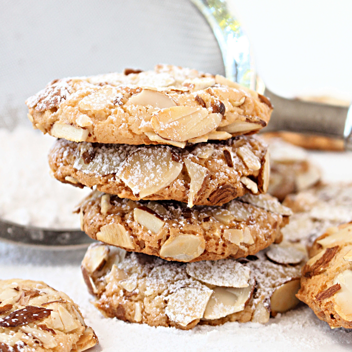 Stack of almond encrusted, golden brown cookies with powdered sugar.